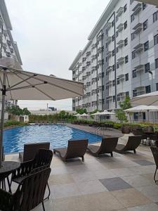 a pool with chairs and an umbrella next to a building at LEAF RESIDENCES MUNTINLUPA - M&G Staycation in Manila