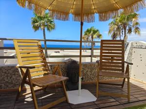 two chairs and an umbrella on a deck with the beach at 100 Steps to the Sand. in La Tejita
