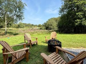 three wooden chairs and a grill in the grass at Luxury Waterfront Retreat I Deluxe Lodge I Private Hot Tub & Sauna in Belturbet