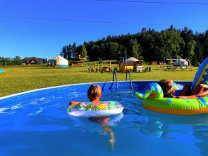 three children are floating on inflatables in a swimming pool at Glamping Niebiańska Osada Jurty Dolnośląskie in Polanica-Zdrój