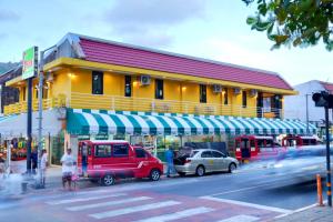 卡伦海滩Bed & Beach Hostel Karon的一条黄色的建筑,在街道前停有汽车