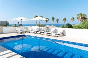 a swimming pool with chairs and umbrellas and the ocean at Villa Cynthiana 4- 300m from the sea 3 bedrooms 3 bathrooms in Kissonerga