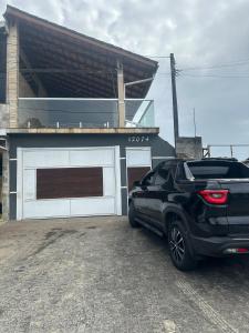 ein schwarzes Auto, das vor einer Garage parkt in der Unterkunft CASA PISCINA CHURRASQUEIRA Wi-Fi BERTIOGA in Bertioga