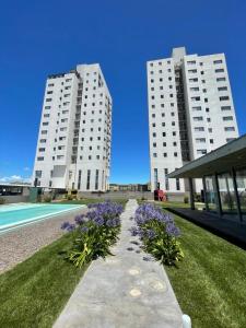 two tall white buildings with purple flowers in the grass at Departamento de lujo con vista al mar in Monte Hermoso