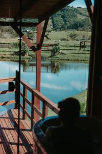 a person sitting in a chair looking out a window at a river at Chalé Rústico com Hidromassagem e Piscina in Imaruí