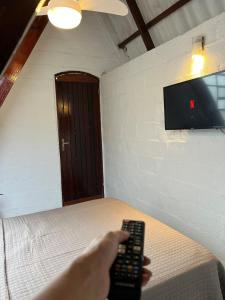 a person holding a remote control in a bedroom at Casa estilo chale dúplex com 3 quartos, churrasqueira, balanço, chuveirão e a uma quadra da praia in Mangaratiba