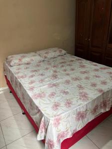 a bed in a bedroom with a pink floral bedsheet at Quarto Confortável in Belém