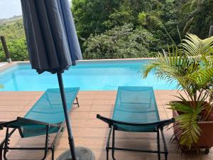 two chairs and an umbrella next to a swimming pool at Tiny house campagne proche plages in Quartier Morne Acajou