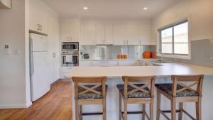 a kitchen with white cabinets and a counter with two bar stools at Grey On The Bay in Coffin Bay