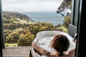 a woman laying in a bath tub looking out a window at the ocean at Sea Dragon Kangaroo Island in Penneshaw