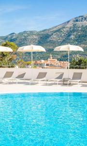 a pool with chairs and umbrellas next to the water at Marko Polo Maradiso Hotel by Aminess in Korčula