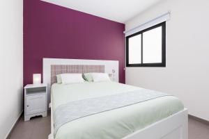 a bedroom with a white bed and a purple wall at Home2Book Modern Apartment Near Playa del Pozo in Puerto del Rosario