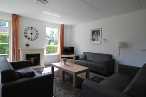 a living room with couches and a table and a clock at Beachvilla Royaal Classic met Sauna - 10 personen in Holle Poarte