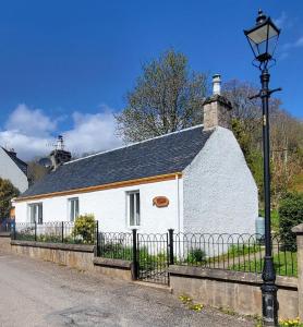 a white building with a black roof and a street light at Ghillies Cottage, Loch Ness in Milton