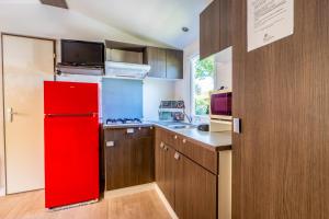 a red refrigerator in a kitchen with wooden cabinets at Mobil home dans camping familial piscine in Sainte-Eulalie-en-Born