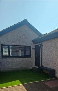 a house with a black door and green grass at Laighdykes Guest Cottage in Saltcoats