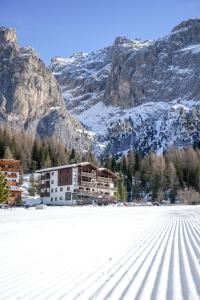 un bâtiment dans la neige devant une montagne dans l'établissement Hotel Wolf, à Selva di Val Gardena