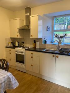 eine Küche mit weißen Schränken und einer Spüle und einem Fenster in der Unterkunft Fordie East Cottage in Comrie