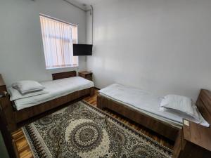 two beds in a room with a rug and a window at Sadaf Hotel in Guliston