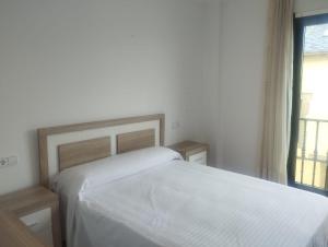 a white bedroom with a bed and a window at Piso Ría de Ribadeo in Ribadeo