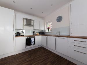 a kitchen with white cabinets and a clock on the wall at Lower Chine Apartment in Shanklin +10 photos