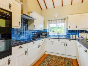 a kitchen with white cabinets and blue tiles at Beudy - Uk31388 in Caeathro +15 photos