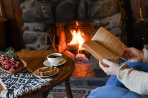 a person reading a book and drinking coffee in front of a fireplace at Hosteria Las Cartas in San Carlos de Bariloche