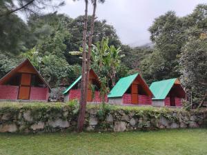a row of red houses with green roofs behind a stone wall at Lucmabamba Cottage in Sahuayacu
