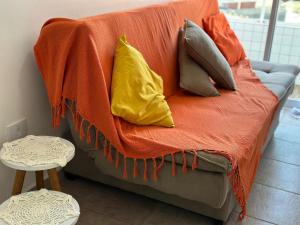 a couch with pillows on it with an orange blanket at Localização Perfeita na Mirim! 100m da Praia! in Samaritá