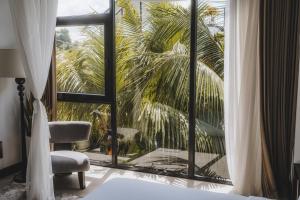 a bedroom with a window with a chair and a palm tree at AMO Residences in Canggu