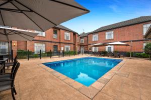 a swimming pool in front of a building with an umbrella at Quest Dandenong in Dandenong