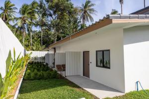 a white house with a garden and palm trees at De Helga Apartment Chaloklum in Ko Phangan
