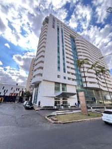 a large white building with palm trees in a parking lot at Mercure Lider 1303, Flats Rocha in Brasilia
