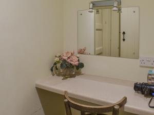 a bathroom counter with a mirror and a vase of flowers at Honeysuckle Cottage in North Mundham