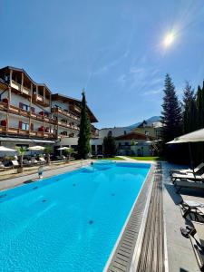 a large swimming pool with chairs and a building at Upside Down Town Hotel Neue Post in Zell am See