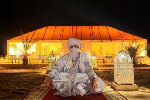 una persona sentada en una alfombra frente a un edificio en Global Luxury Camp, en Merzouga