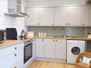 una cucina con mobili bianchi, lavatrice e asciugatrice di Moss Cottage a Burry Port