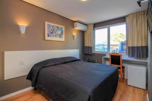 a bedroom with a bed and a desk and a window at Coral Express próximo ao Parque Harmonia e Beira Rio in Porto Alegre