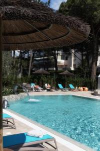 uma piscina com um guarda-sol e algumas cadeiras e cadeiras em Hotel Arizona em Lignano Sabbiadoro