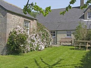 a house with a yard with a bench and flowers at Honeysuckle Cottage - 23227 in Embleton
