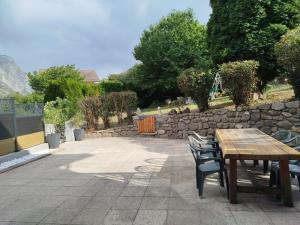 a patio with a wooden table and chairs and a stone wall at Appartement avec terrasse au pied des cols et des stations de ski in Villargondran +2 photos