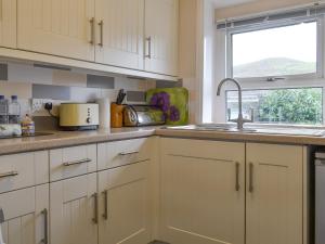 Una cocina con gabinetes blancos y un fregadero y una ventana. en Isallt, en Nantlle