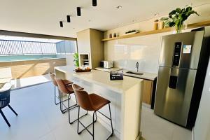 a kitchen with a counter with chairs and a refrigerator at Loft, House próximo ao Center Shopping in Uberlândia