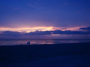 a sunset on the beach with people walking on the beach at Inn at Pelican Bay in Naples