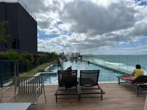 2 personnes assises sur des chaises en face d'une piscine dans l'établissement Lindo studio frente mar!, à Salvador