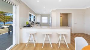 a kitchen with white countertops and stools at Ettalong Waterfront Retreat in Ettalong Beach +15 photos