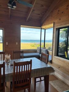 une salle à manger avec une table, des chaises et des fenêtres dans l'établissement Bella Vista on the Beach, à Matarangi
