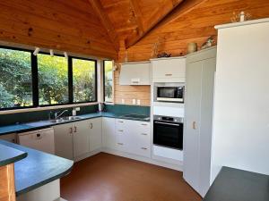 a kitchen with white cabinets and a wooden ceiling at Bella Vista on the Beach in Matarangi +10 photos
