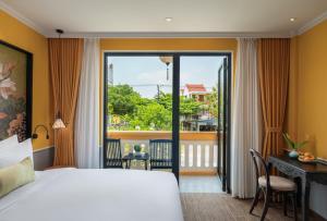 a bedroom with a bed and a desk and a balcony at Sen Village Hoi An in Hoi An +52 photos