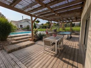 eine Holzterrasse mit einem Tisch und einer Pergola in der Unterkunft Maison de vacances raffinée avec terrasse et piscine partagée - FR-1-589-837 in Dounoux